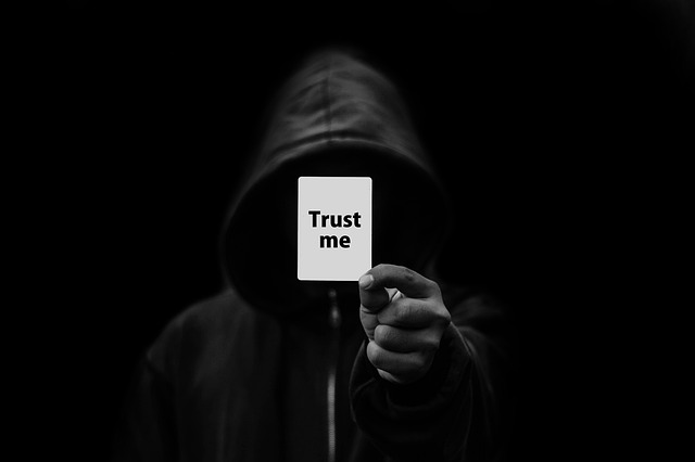 člověk v kapuci ukazující ze tmy kartičku s nápisem trust me